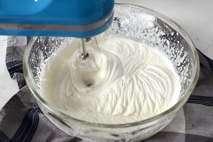 Whipping cream being beaten in a large glass bowl