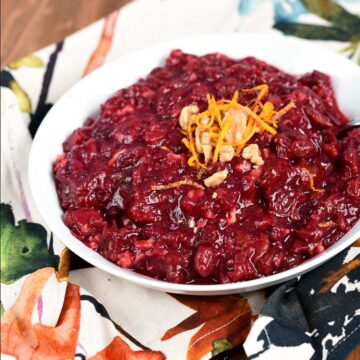 A white bowl filled with Cranberry Sauce with Pineapple and topped with orange zest and chopped walnuts