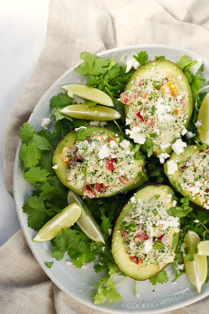 Looking down on four Healthy Tuna Stuffed Avocado halves sitting on a bed of cilantro leaves and lime wedges