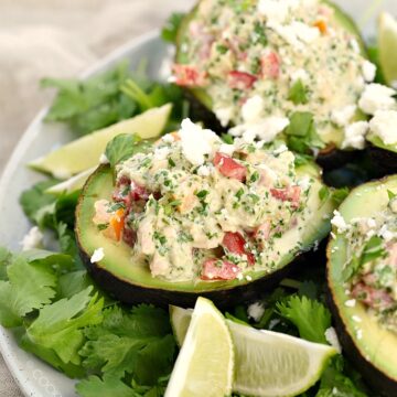 Healthy Tuna Stuffed Avocado sitting on a bed of cilantro leaves with lime wedges