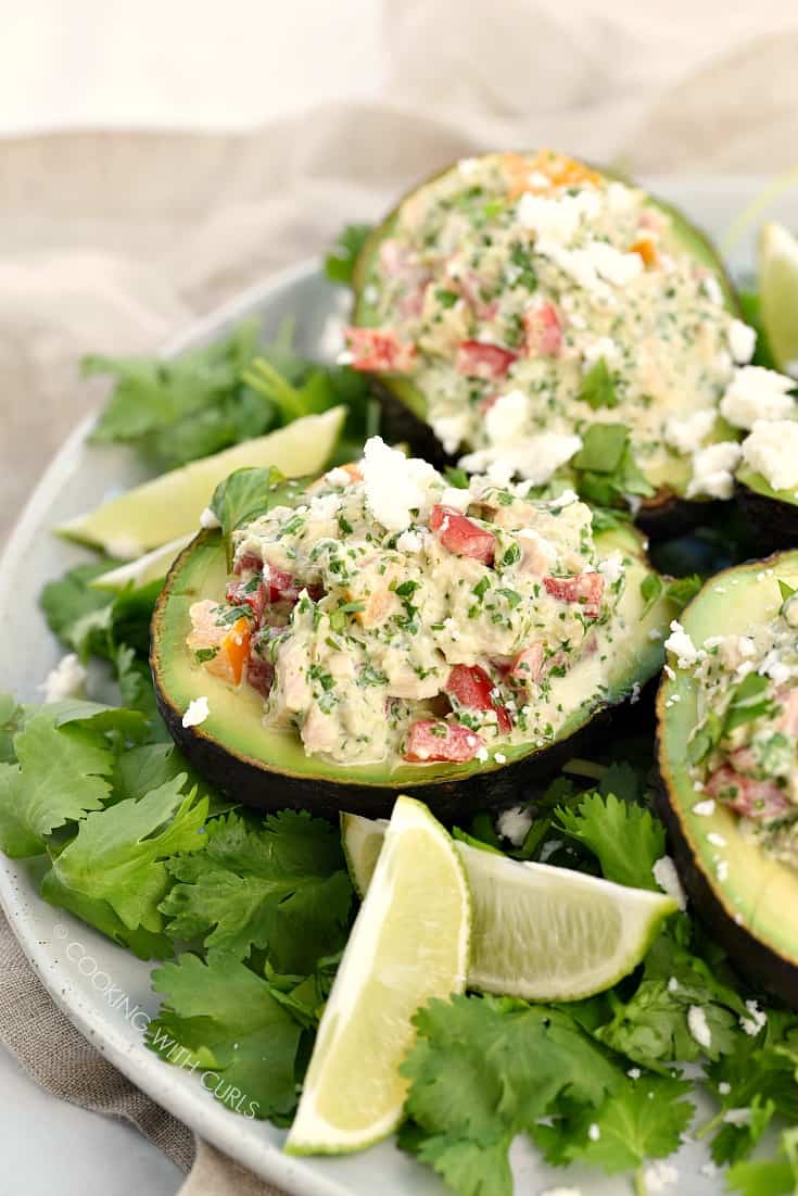 Healthy Tuna Stuffed Avocado sitting on a bed of cilantro leaves with lime wedges