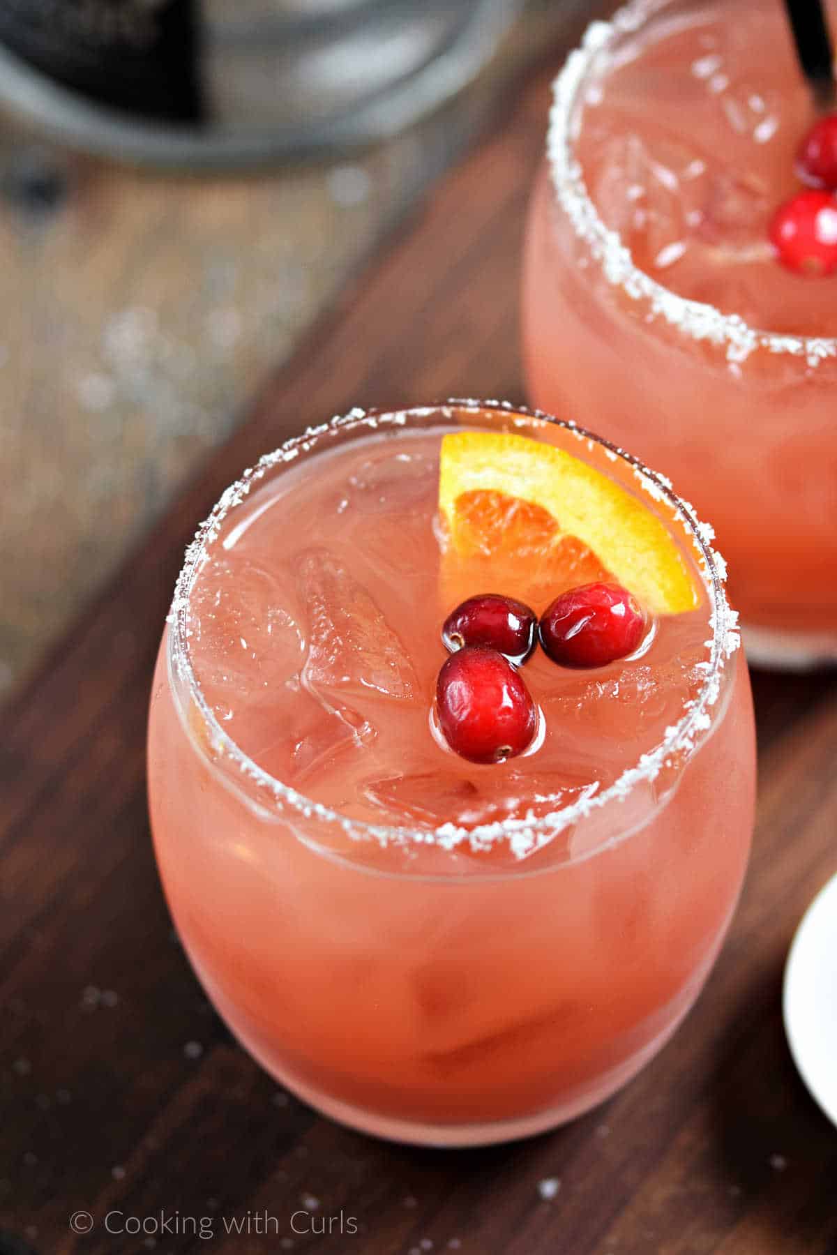 Two cranberry orange margaritas salt rimmed glasses with an orange wedge and three cranberries.