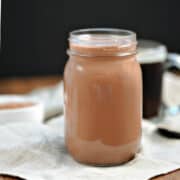 Peppermint mocha creamer in a mason jar with a cup of coffee in the background.