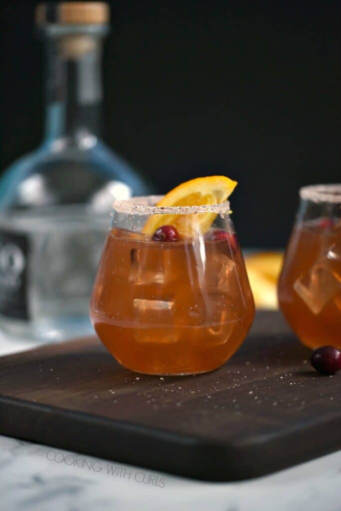 Side view of two glasses filled with Cranberry Orange Margarita and garnished with orange wedge and fresh cranberries