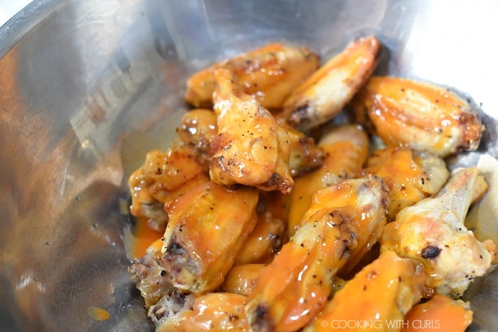 Baked chicken wings tossed with buffalo sauce in a large bowl. 