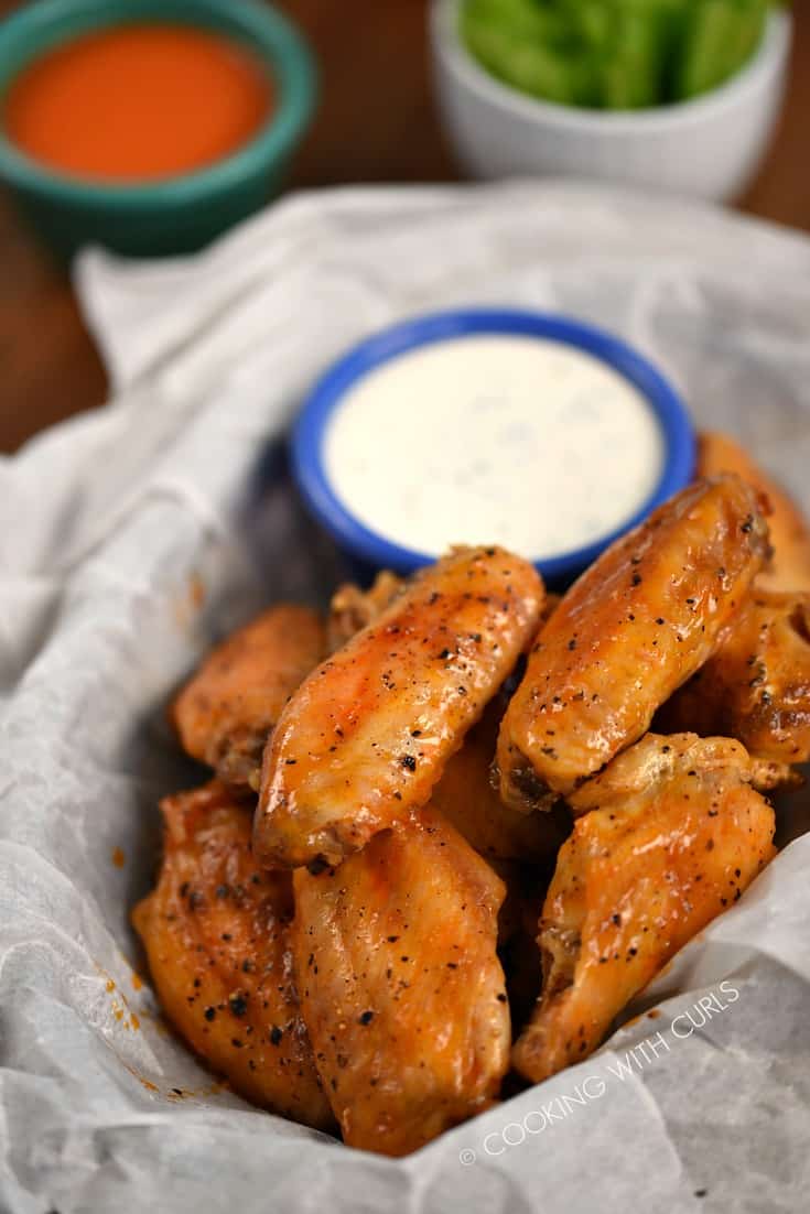 A basket filled with Baked Buffalo Chicken Wings with a side of ranch dressing, hot sauce and celery sticks.