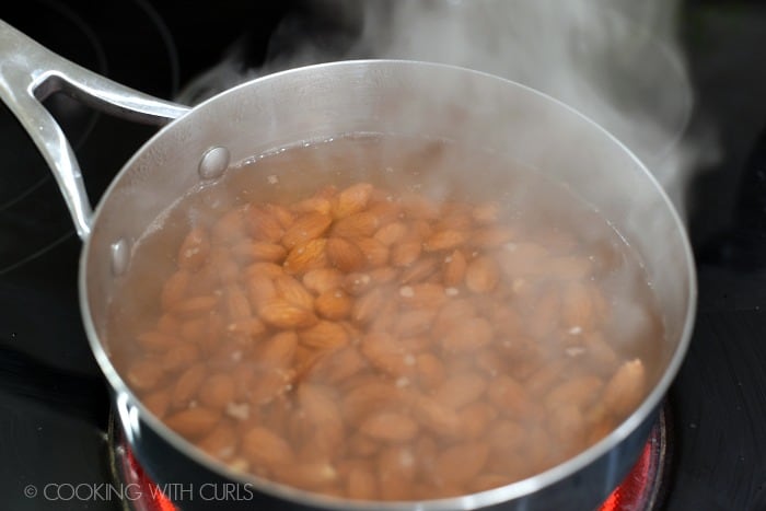 Raw almonds added to the boiling water in the saucepan. 