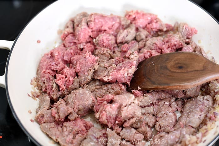 Raw ground beef added to the garlic and onions in a large skillet.