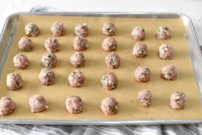 Raw, pork meatballs lined up on a parchment lined baking sheet 