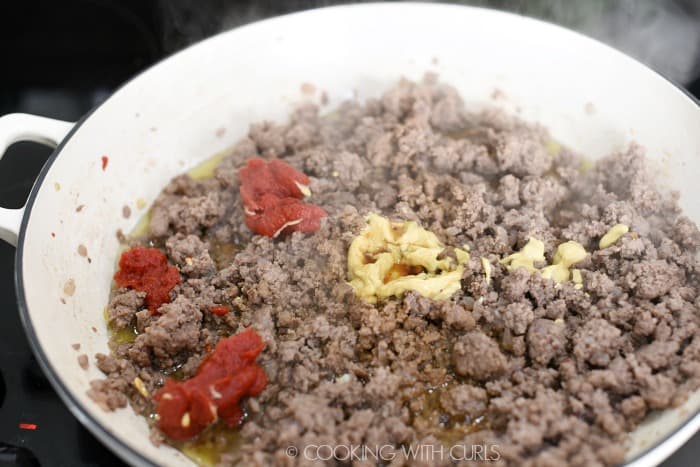 Tomato paste and mustard added to the cooked ground beef in a large skillet.
