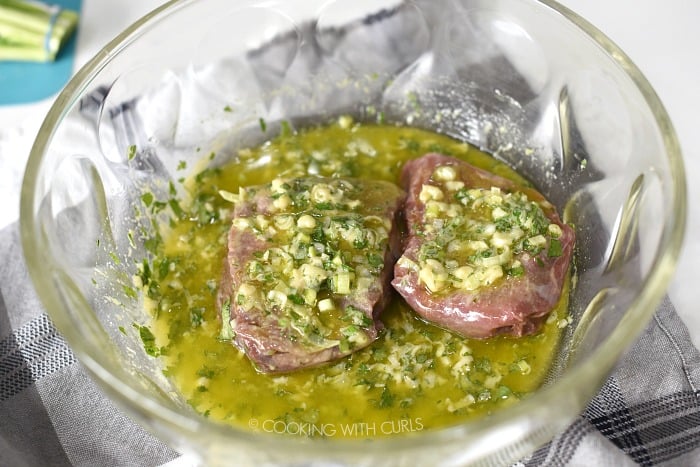 Two sirloin steaks in cilantro-lime marinade in a large glass bowl. 