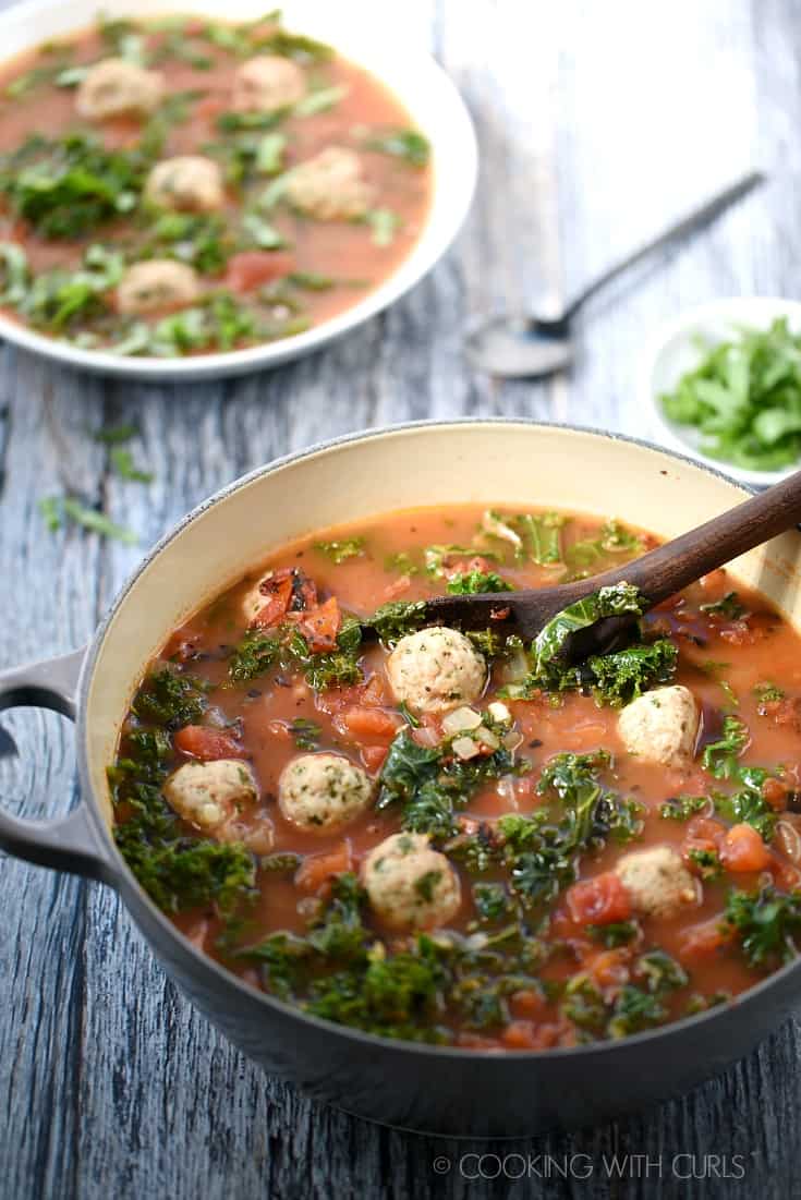 A big pot of Italian Meatball Soup with a wooden spoon and a bowl of soup in the background