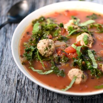 A bowl of Italian Meatball Soup with a second bowl of soup and a dish of basil in the background