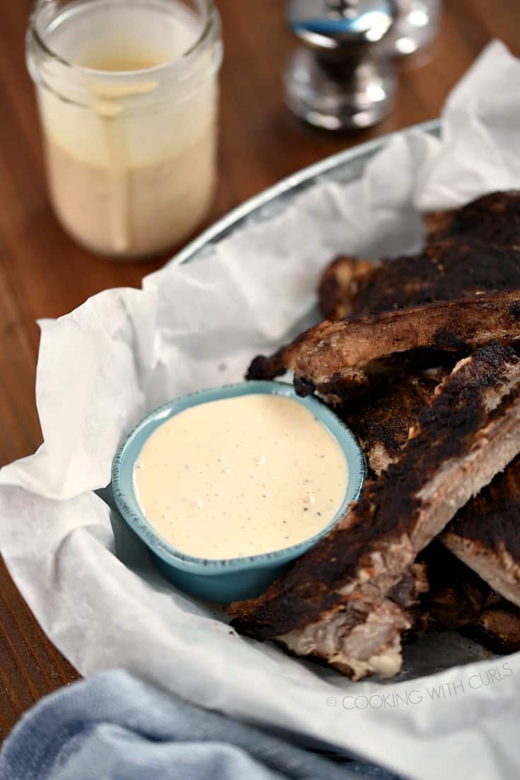 A basket of ribs with a side of Alabama White Barbecue Sauce in a small blue bowl.