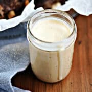 A jar filled with Alabama White Sauce with a basket of ribs in the background.
