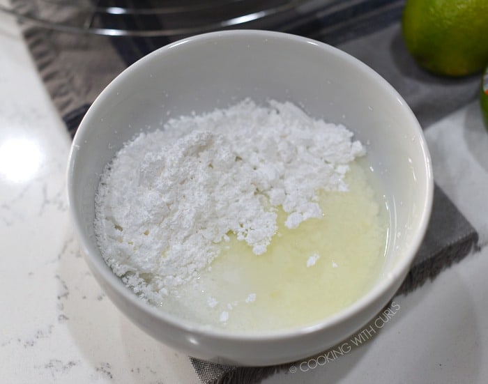 Powdered sugar, tequila, lime juice and orange liqueur in a small white bowl. 