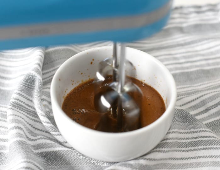 A blue hand mixer beating the coffee mixture together in a small, deep bowl. 