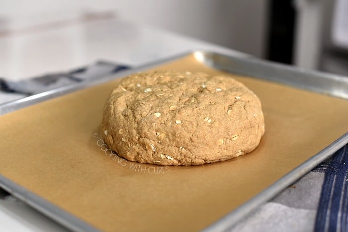 Bread dough shaped into a circle on a parchment lined baking sheet. 