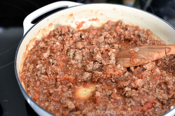 Crushed tomatoes stirred into the ground beef mixture with a wooden spoon. 