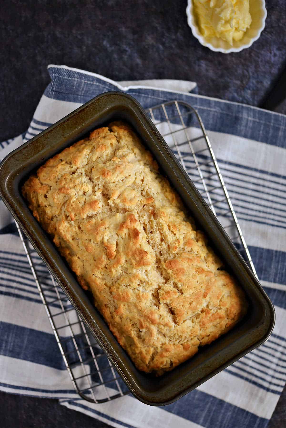 Baked beer bread in a loaf pan sitting on a wire rack.