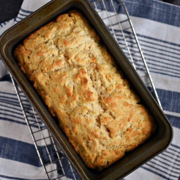 Beer bread in a loaf pan sitting on a wire rack.