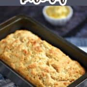 A golden brown loaf of beer bread in a loaf pan sitting on a wire rack with title graphic across the top.