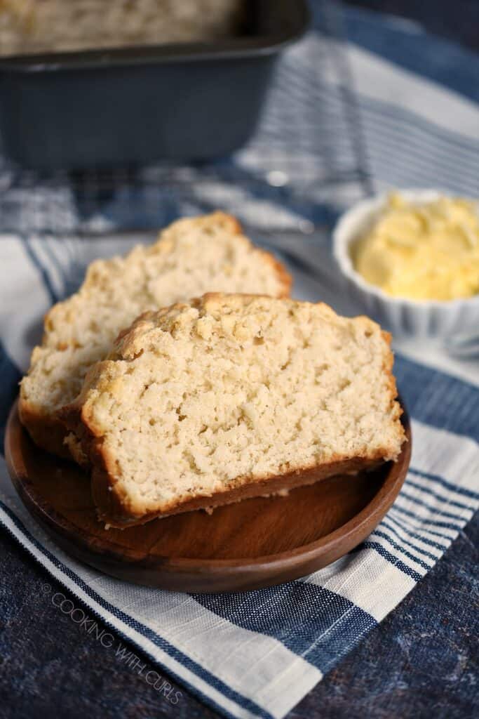 Closeup image of two slices of Homemade Beer Bread on a wood plate with a bowl of butter in the background.