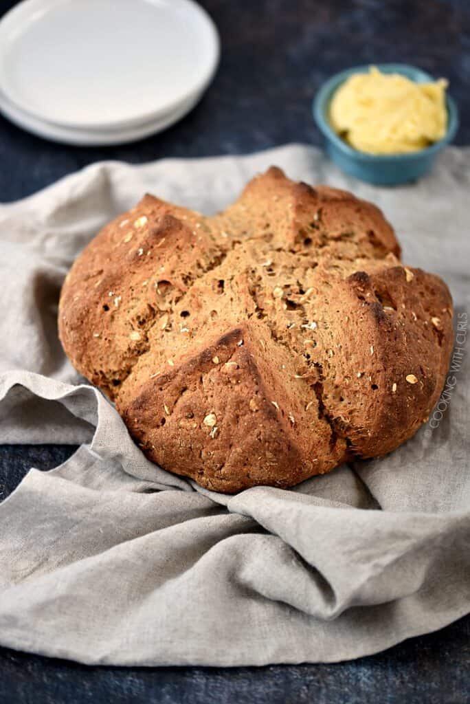 Irish Brown Soda Bread on a beige napkin with plates and softened butter in the background.