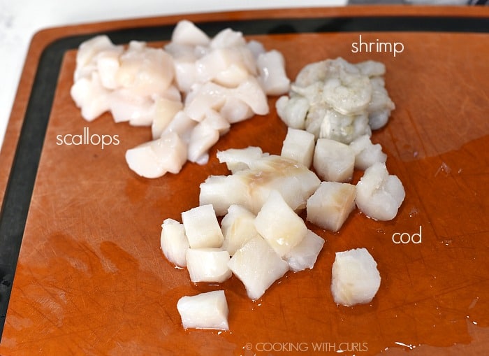 Quartered scallops, raw shrimp and diced cod on a cutting board. 