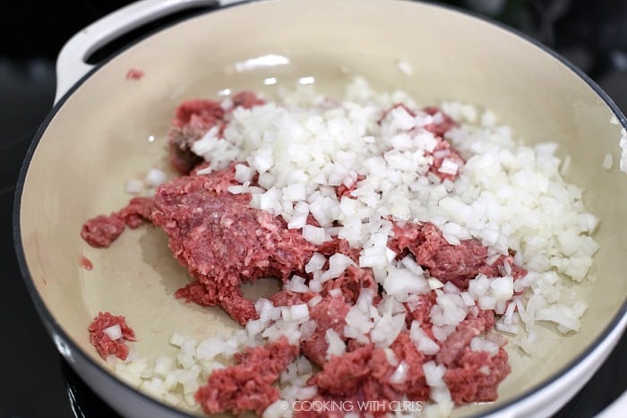 Raw ground beef and diced onions in a cast iron casserole skillet. 