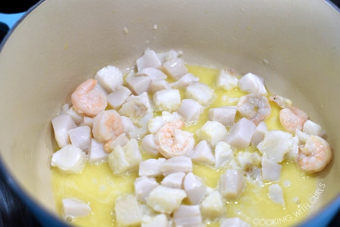 Shrimp, scallops and cod cooked in butter in a large pan. 