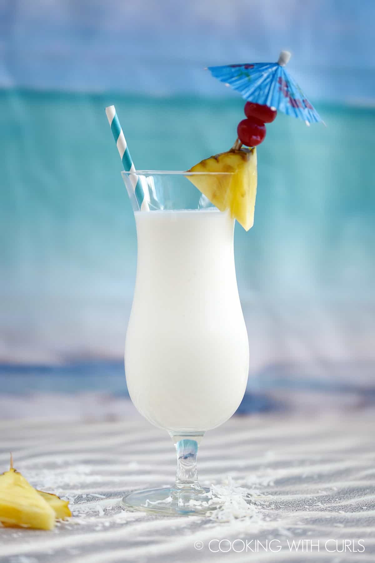 Creamy Pina Colada Milkshake in a hurricane glass garnished with a pineapple wedge, two cherries and a blue umbrella.