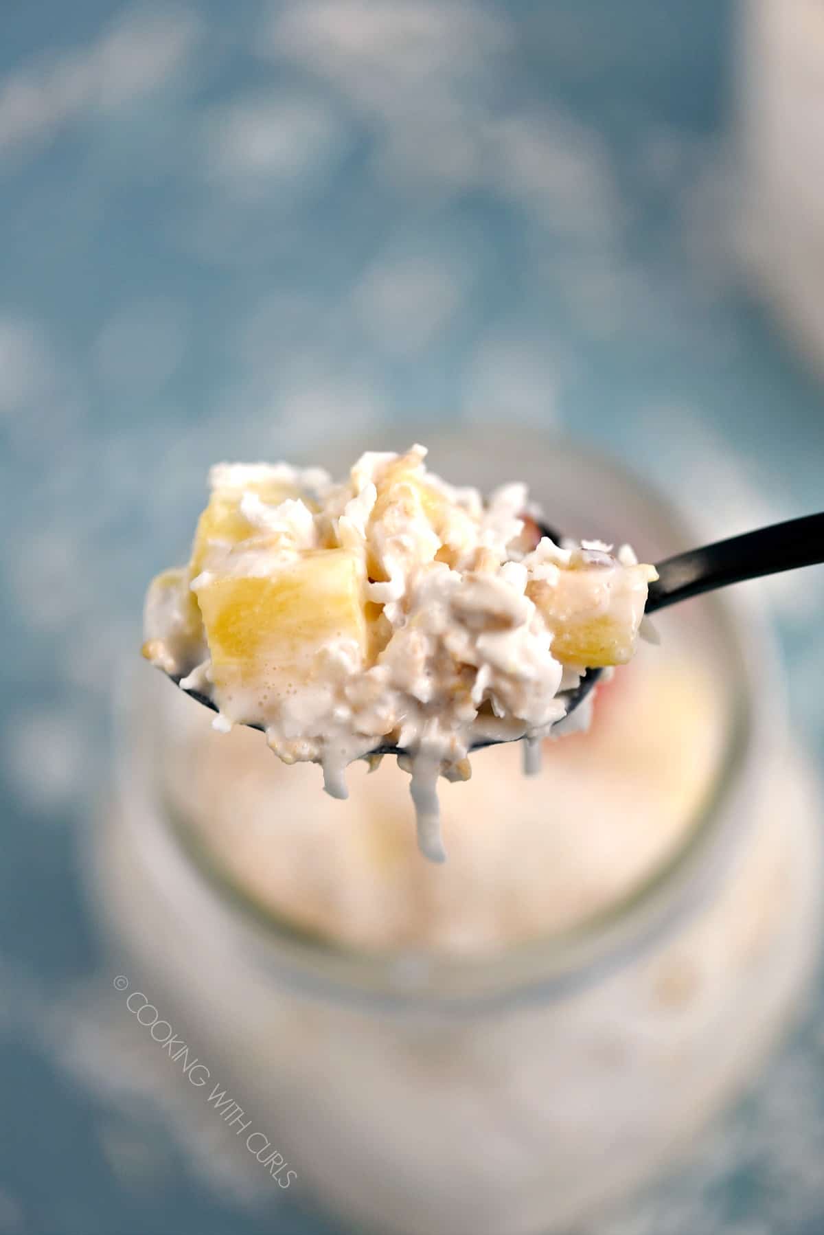 A spoonful of Pina Colada Overnight Oats scooped out of a glass mason jar. 