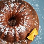 Bundt cake topped with coconut flakes on a wood cake plate with pineapple wedges on the edge.