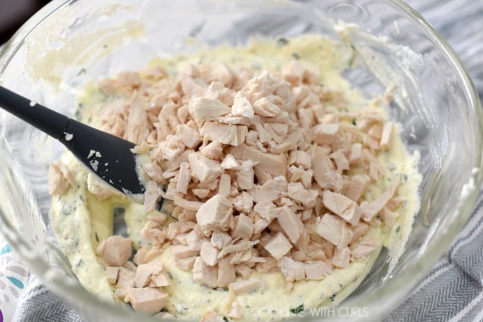 Chopped chicken stirred into ricotta mixture with a gray spatula in a glass bowl.