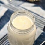 Looking down on a glass jar filled with Classic Alfredo Sauce sitting on a blue and white striped napkin with title and wedge of Parmesan at the top of the image.