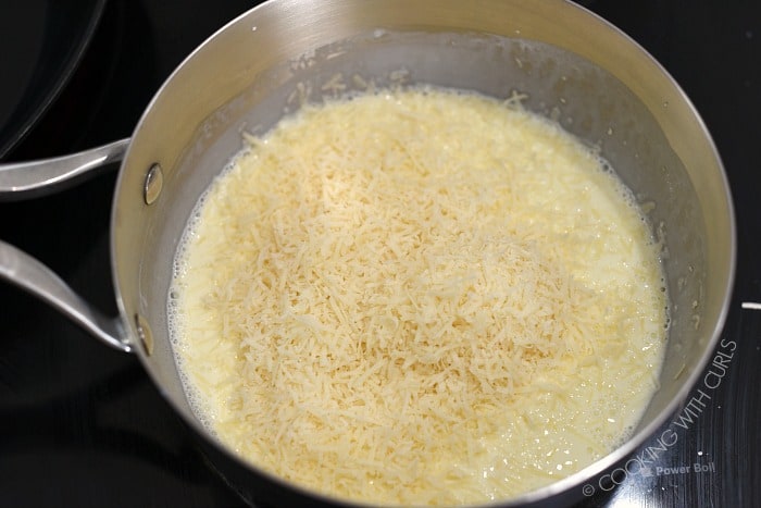 Grated parmesan added to the simmering cream and butter in a saucepan. 