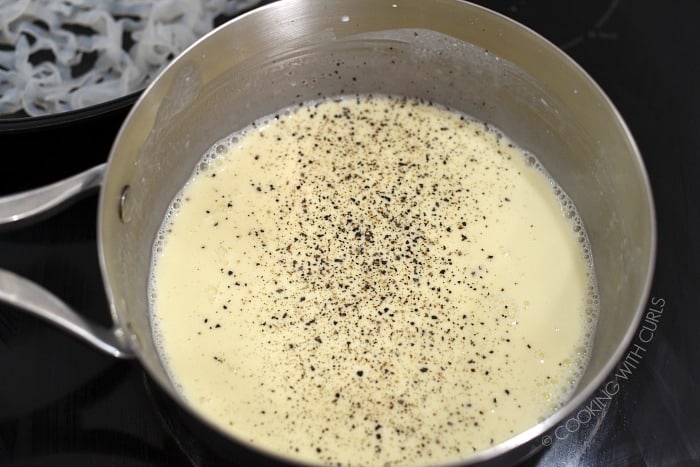 Ground pepper added to the Classic Alfredo Sauce on the stove top in a saucepan. 