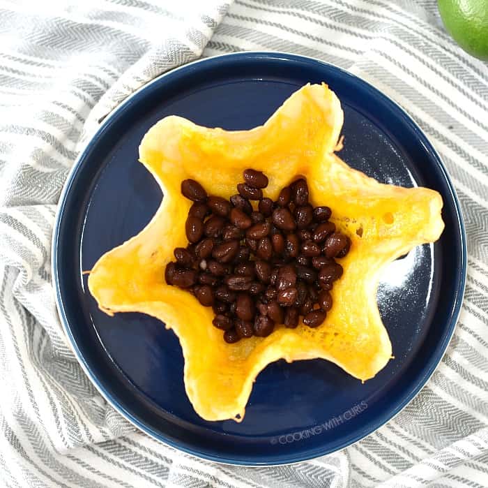 Melted cheese topped tortilla shell with black beans sitting on a dark blue plate. 