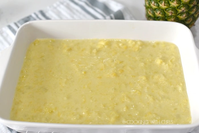 Pineapple filling poured over the cookie base in a white baking dish. 