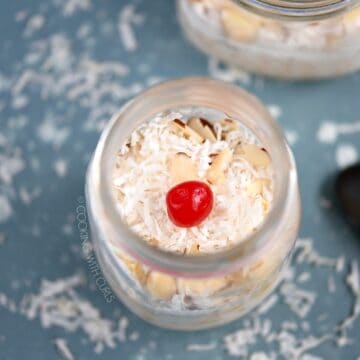 Looking down on a glass mason jar filled with Pina Colada Overnight Oats and topped with a cherry.