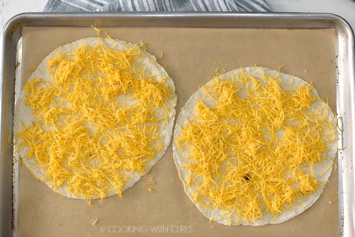 Two flour tortillas topped with grated cheddar cheese. 