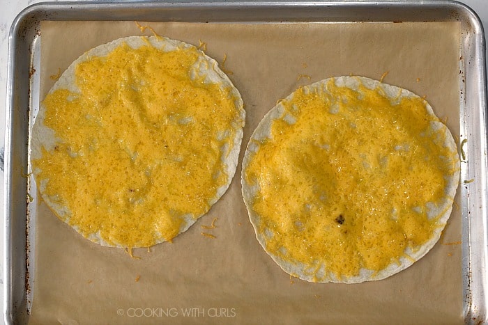 Two flour tortillas with melted cheddar cheese on a parchment lined baking sheet. 