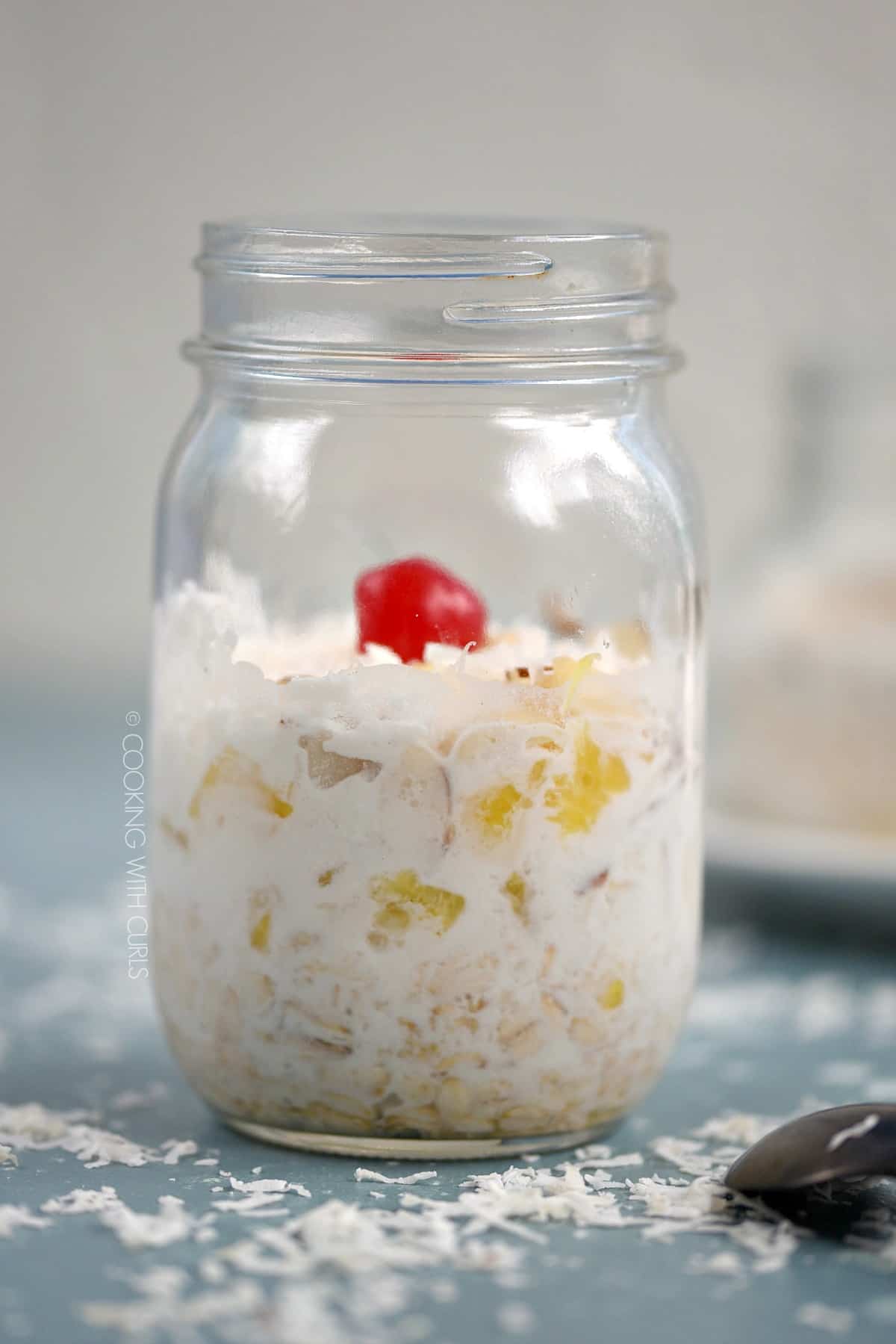 A side view of a glass mason jar layered with Pina Colada Overnight Oats.