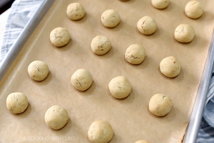 Rows of baked cookie balls on a parchment lined baking sheet. 