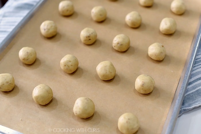 Rows of rolled cookie balls on a parchment lined baking sheet. 