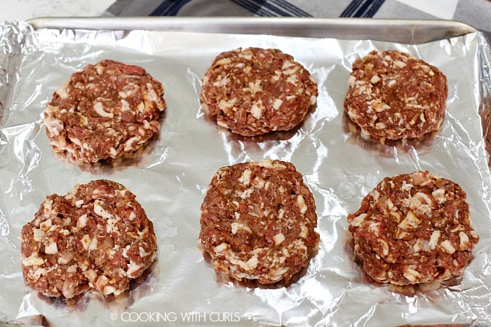 Six bacon burger patties on a foil lined baking sheet.