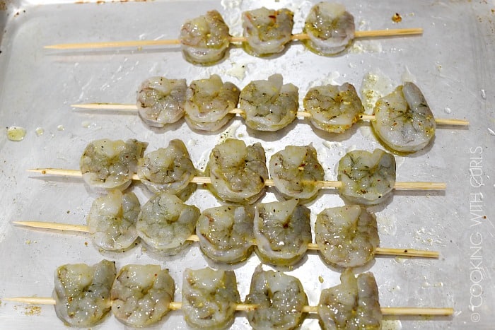 23 Jumbo shrimp on 5 bamboo skewers brushed with seasoned oil mixture laying on a baking sheet. 