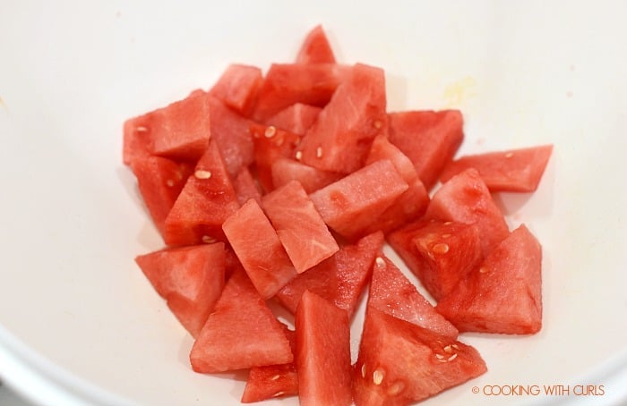 Bite-sized watermelon wedges in a large white mixing bowl. 