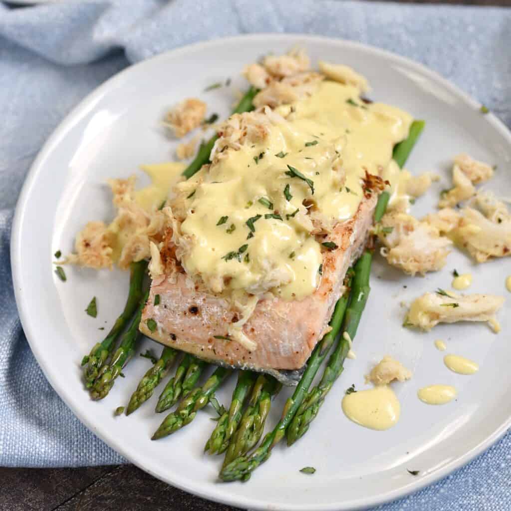 a salmon filet on a bed of asparagus spears topped with crab meat and hollandaise sauce.
